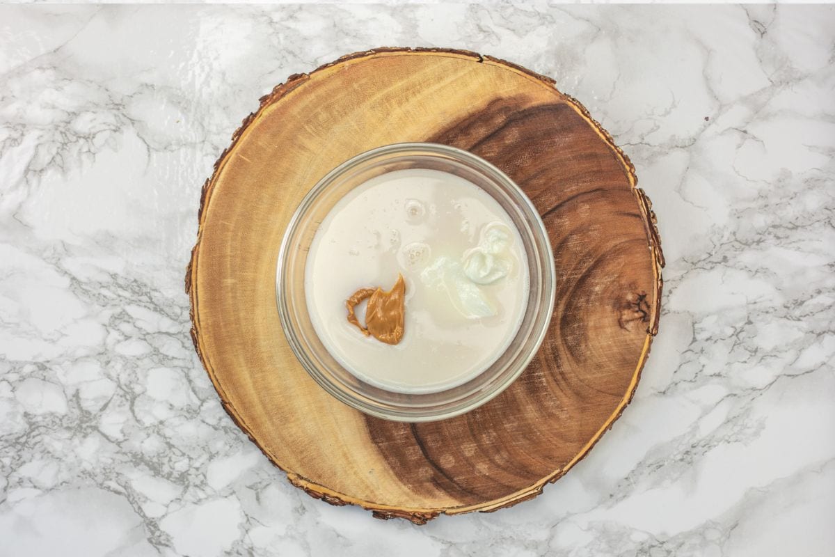 Almond milk, green yogurt, maple syrup and peanut butter added in a bowl.