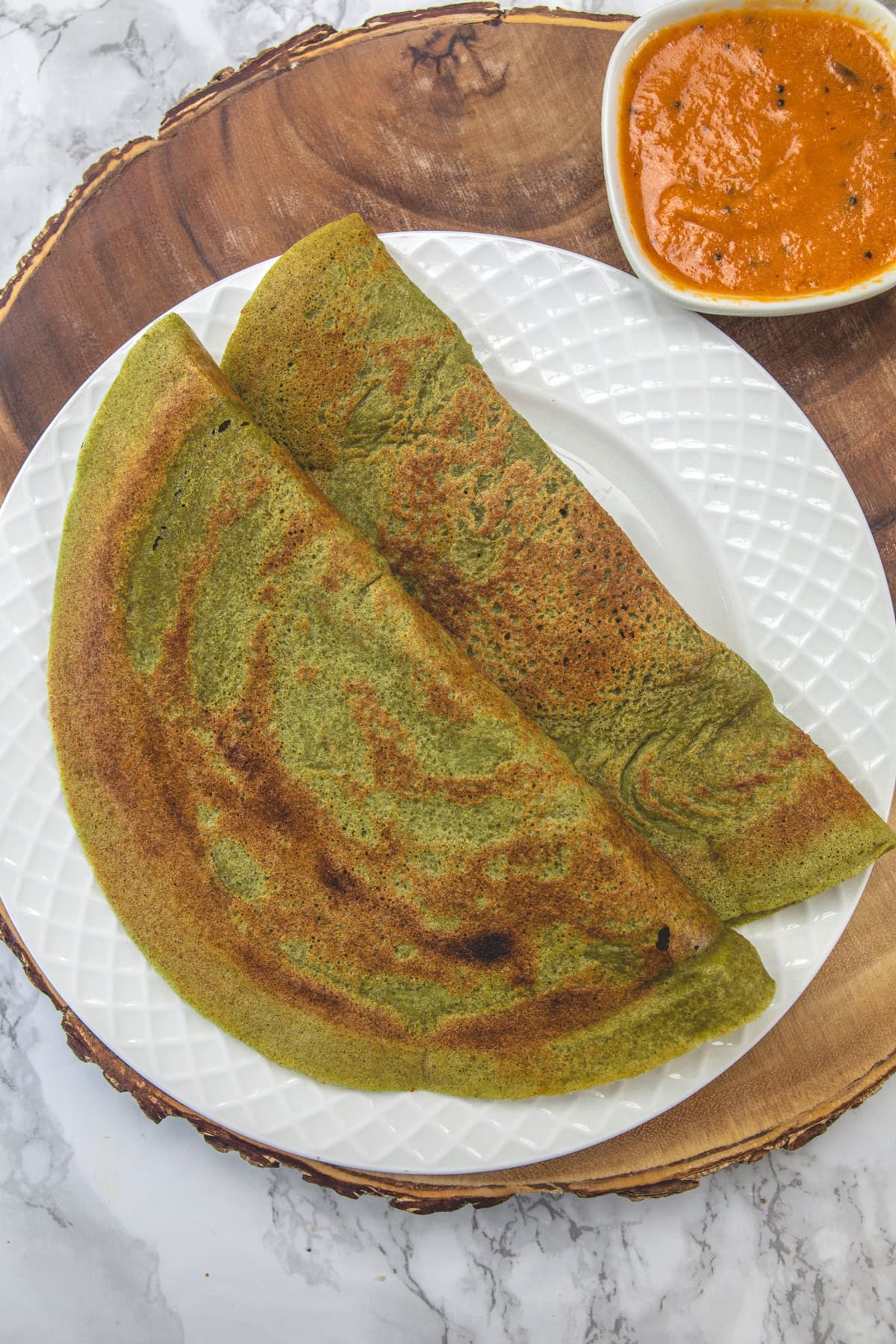 2 Pesarattu served in a white plate with a small bowl of chutney in the back.