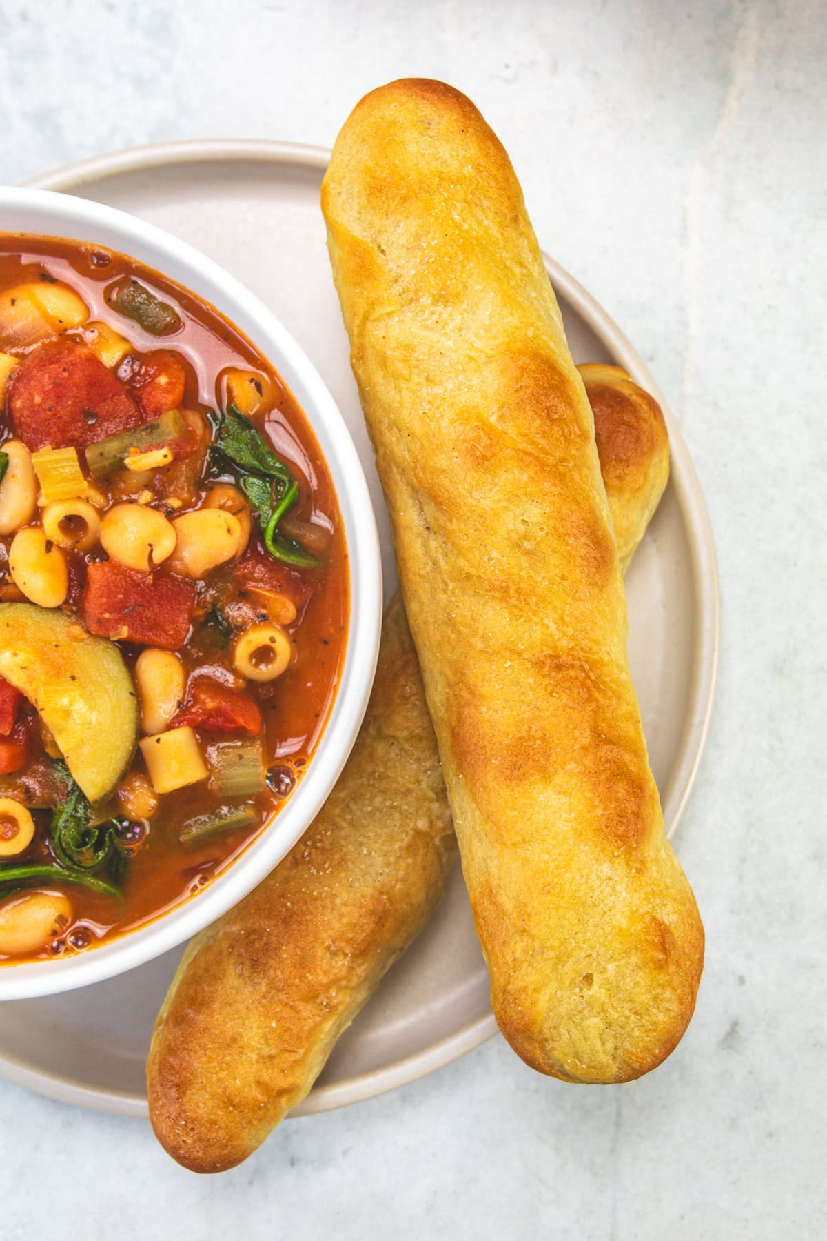 2 copycat Olive Garden breadsticks served in a plate with a bowl of soup.