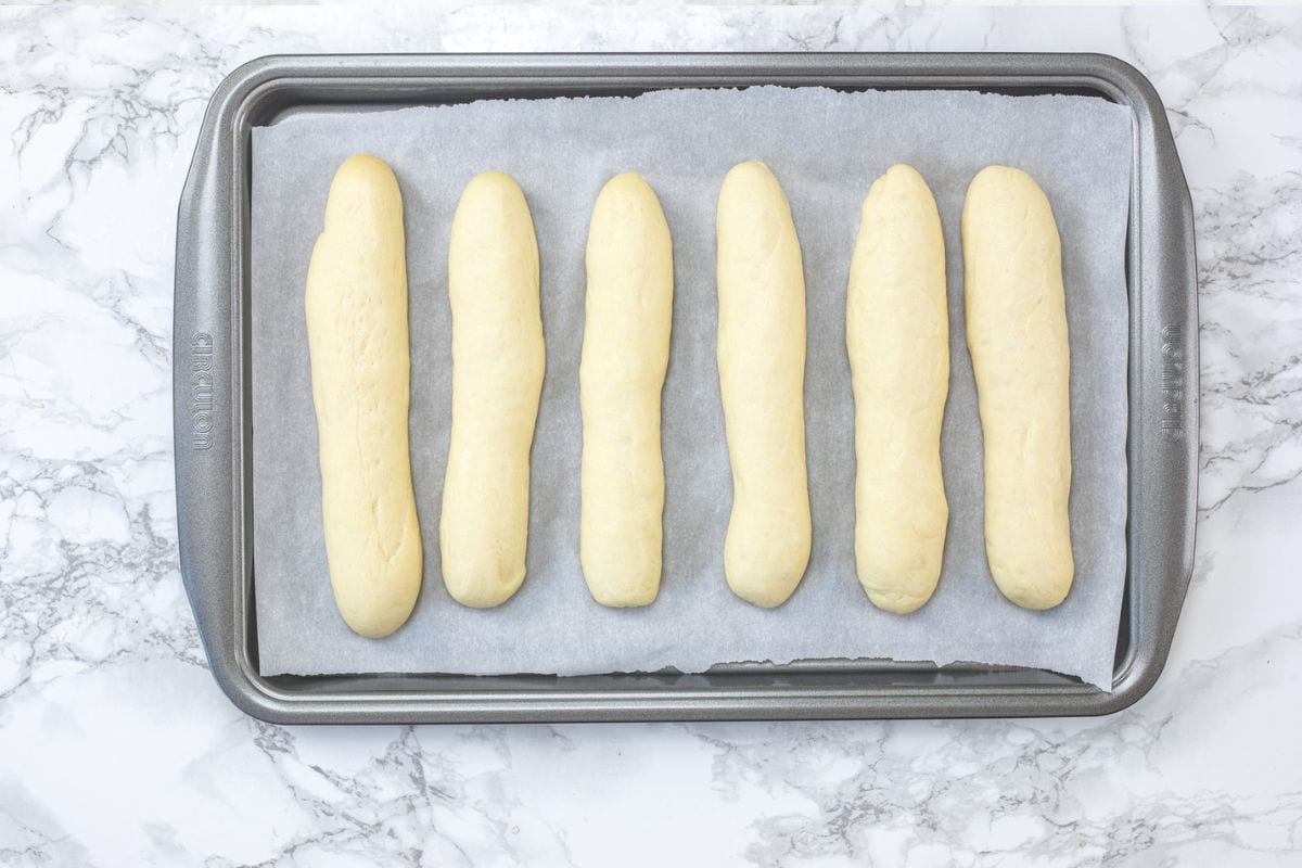 Proofed breadsticks in a baking tray.